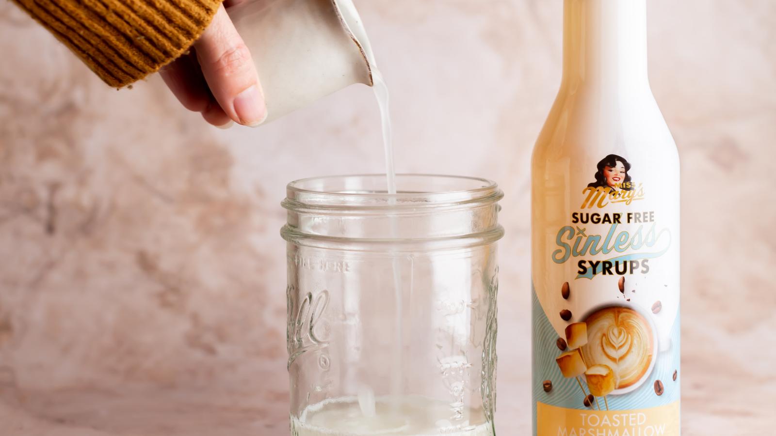 pouring toasted marshmallow sinless syrup into a mason jar for iced coffee