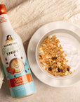Miss Mary's Salted Caramel Sugar-Free coffee syrup and yogurt with granola on light brown table.