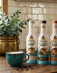 Three bottles of Sugar Free Sinless Syrups on a wooden surface with a teal mug and coffee beans.