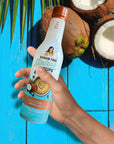 Hand holding a bottle of Sugar Free Girlada coconut syrup against a blue background with coconuts.