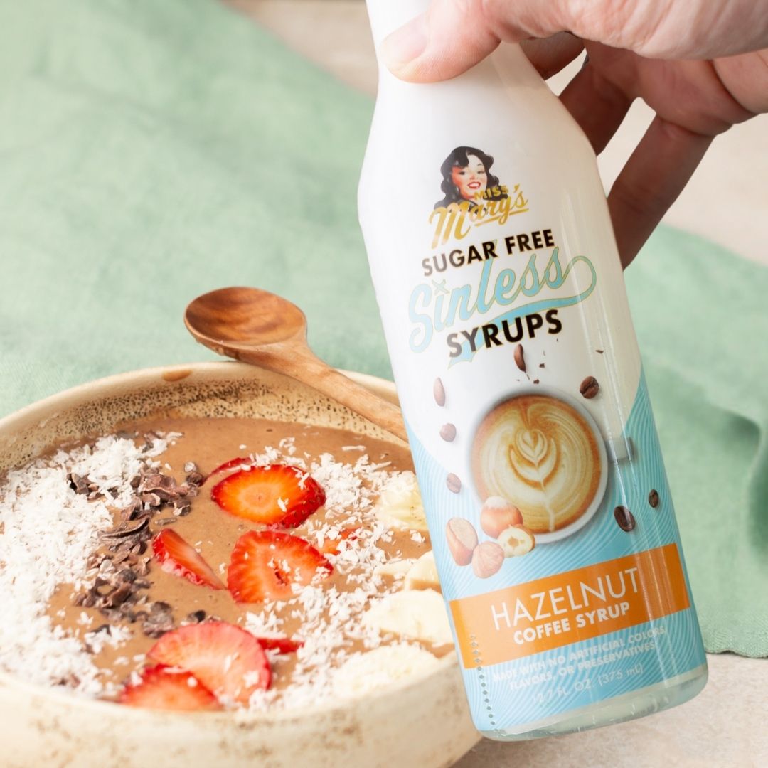 Bottle of Hazelnut Sugar Free Sinless Syrups held over a protein bowl with fruit and coconut.