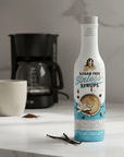 Bottle of Sugar Free Sinless Syrups Madagascar Vanilla Coffee Syrup on a kitchen counter with a coffee cup and coffee maker.