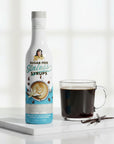 Sugar Free Madagascar Vanilla Sinless Syrup bottle with black coffee and vanilla bean on white background