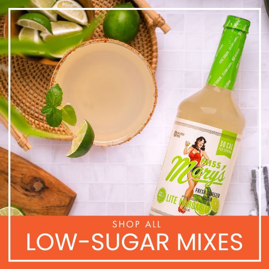 Bottle Miss Mary's lite margarita mix with fresh margarita and limes on a white surface, promoting low-sugar mixes.