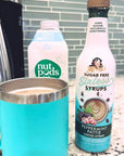 A turquoise insulated coffee mug filled with coffee sits on a granite countertop next to a bottle of Mary's Sugar Free Sinless Syrups Peppermint Pattie Coffee Syrup and a carton of Nut Pods Vanilla.