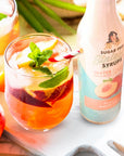 Peach cocktail with a bottle of Peach sugar-free syrup on a white surface