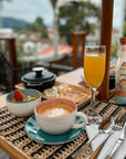Breakfast setting with coffee, fruit, orange juice, and salted caramel Sinless Syrup on a table with a blurred outdoor background.