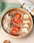 A chocolate smoothie bowl with sliced strawberries, banana, coconut flakes, and chocolate chips, styled with a green cloth and Miss Mary's Salted Dark Chocolate Sinless Syrup