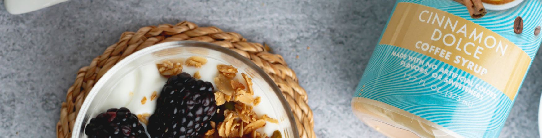 blackberry yogurt parfait next to a cinnamon dolce Sinless Syrup on  gray surface.