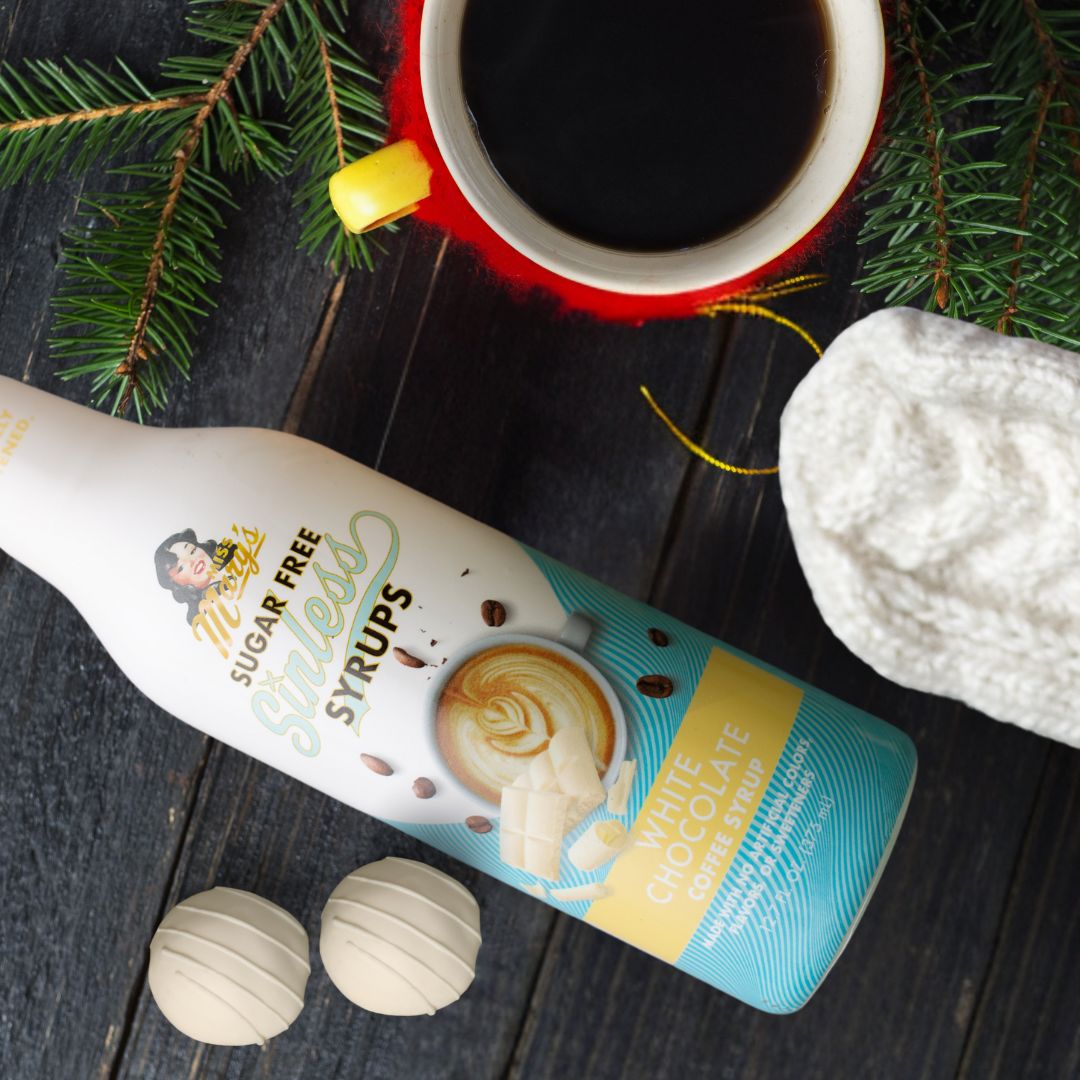 Sugar-free white chocolate Sinless syrup bottle with a holiday cup of coffee and evergreen decor