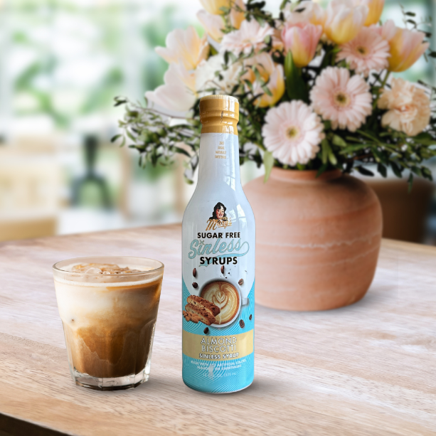 Bottle of Sugar Free Syrups on a table with a glass of iced coffee and flowers in the background