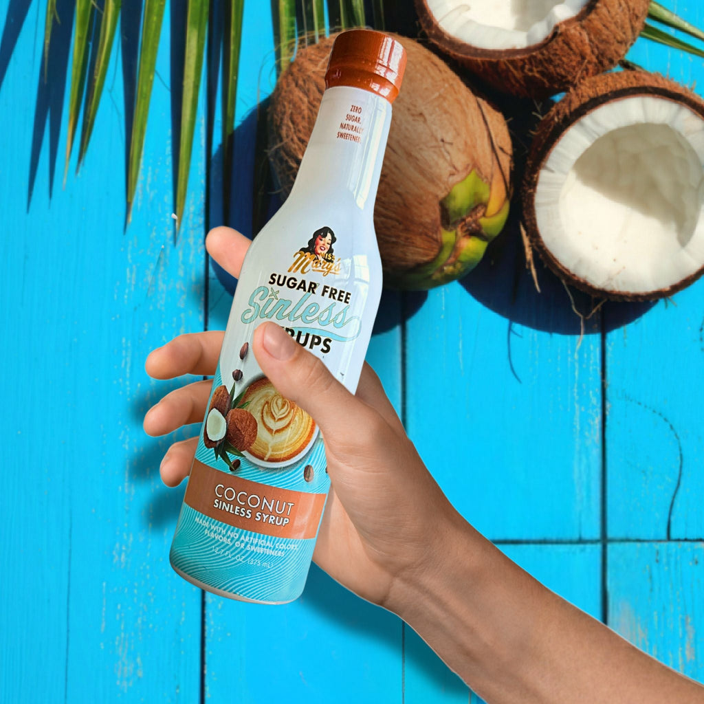 Hand holding a bottle of Sugar Free Girlada coconut syrup against a blue background with coconuts.