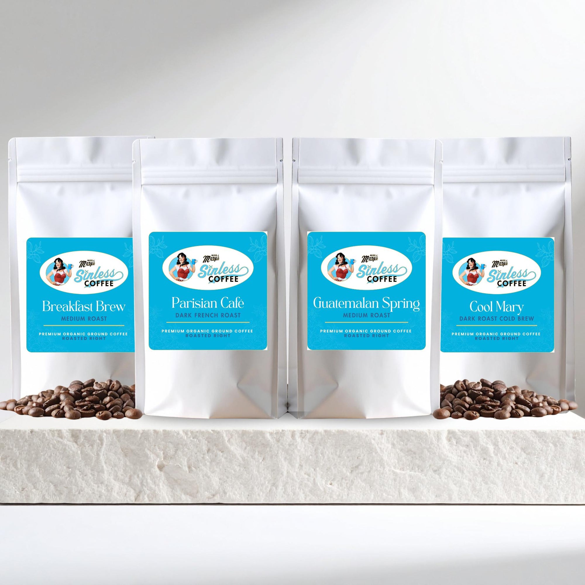 Four white coffee bags with blue labels on a white surface with coffee beans.
