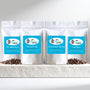 Four white coffee bags with blue labels on a white surface with coffee beans.