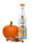 Bottle of pumpkin spice coffee syrup with a pumpkin, nuts, and cinnamon sticks on a white background