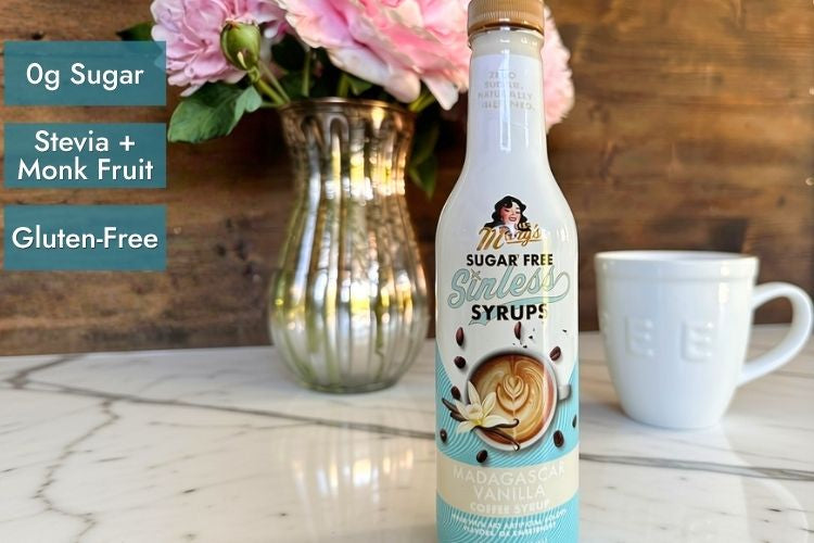 Sinless Syrup bottle in Madagascar Vanilla on marble counter with white coffee mug and vintage glass vase of pink flowers with attributes '0g sugar,' 'stevia+monk fruit,' 'gluten-free'