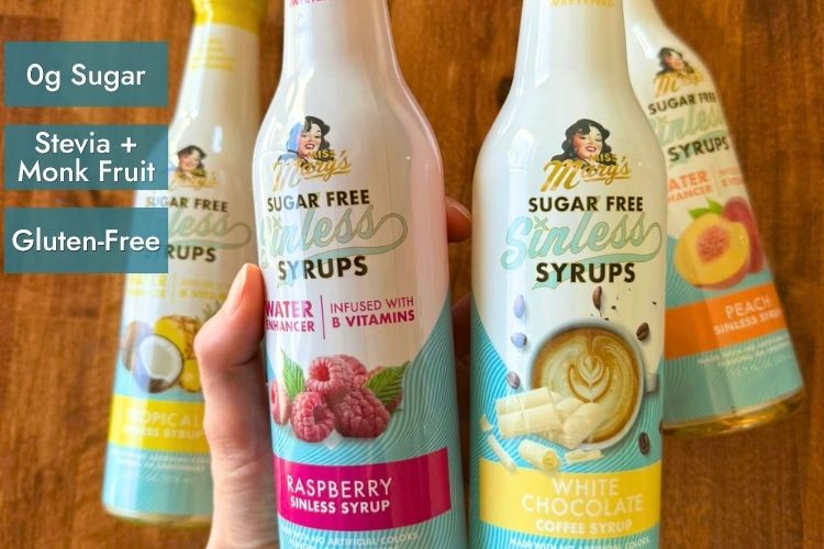 Raspberry Sugar Free Sinless Syrup and others with text "0g Sugar, Stevia + Monk Fruit, Gluten-Free" on wood table.