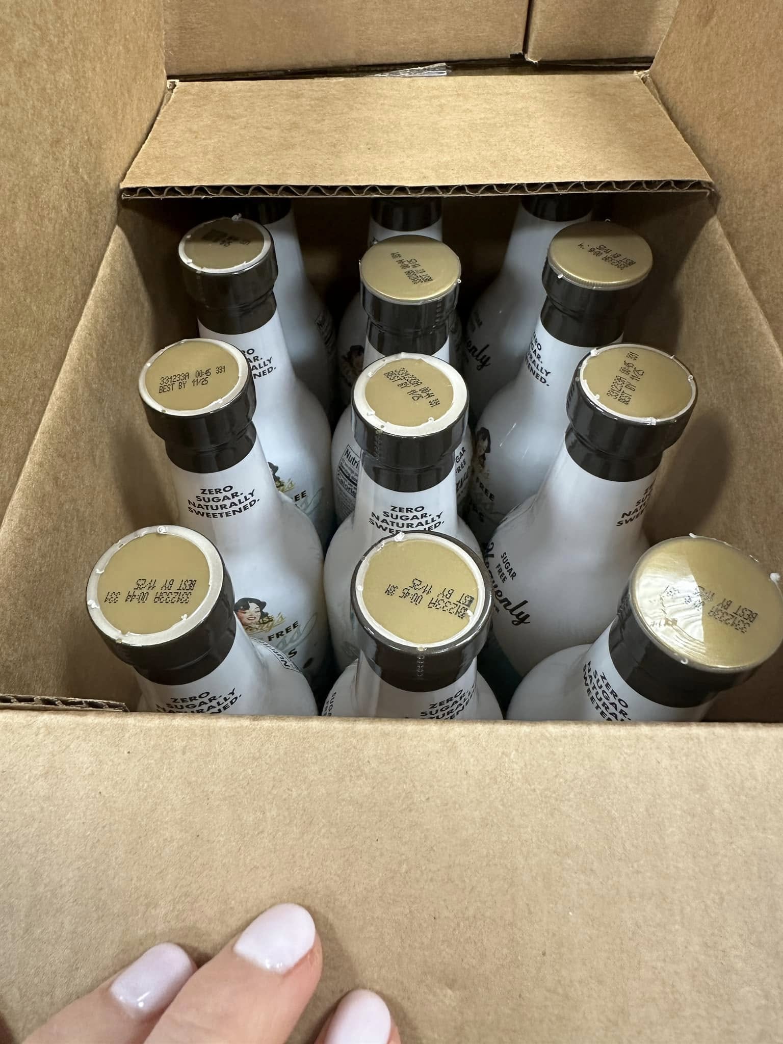 Box containing multiple white bottles with black caps, held by a hand.