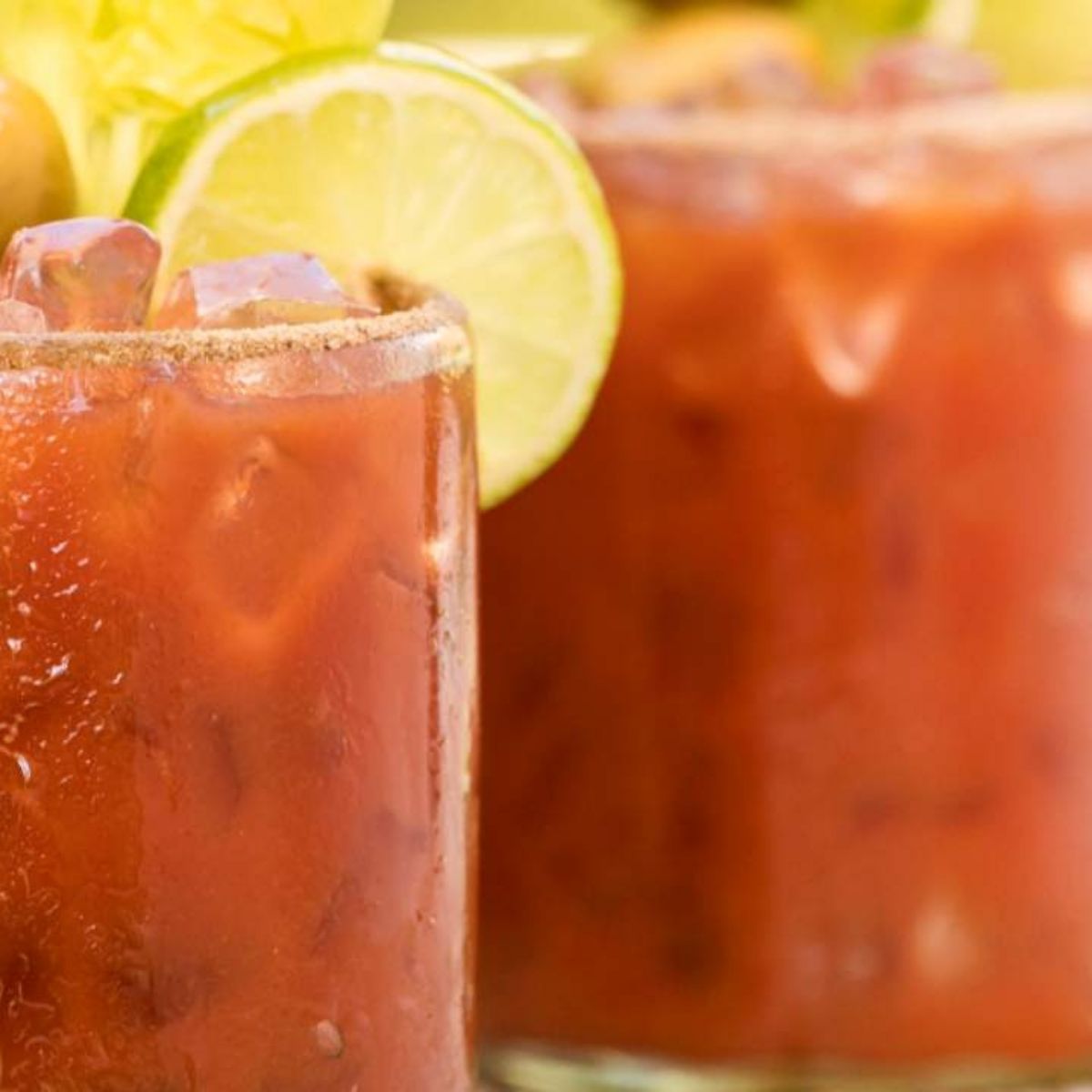 Two glasses of red Bloody Mary cocktails with lime wedges and ice cubes.