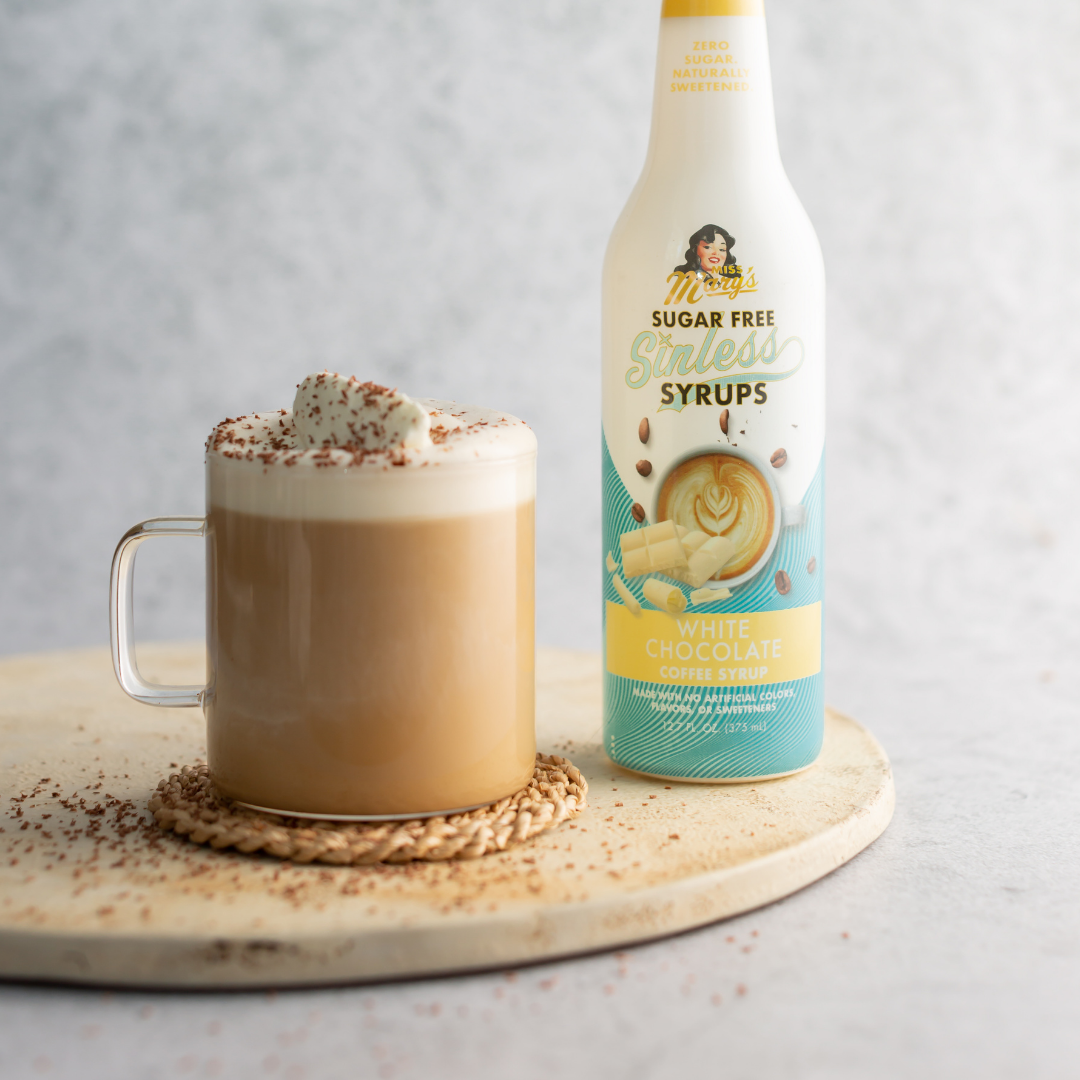 Mocha drink with whipped cream and a bottle of sugar-free syrup on a wooden coaster.