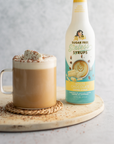 Mocha drink with whipped cream and a bottle of sugar-free syrup on a wooden coaster.