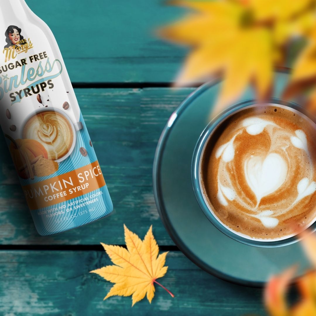 Sugar Free pumpkin spice coffee syrup bottle next to a cup of coffee on a teal surface with autumn leaves.