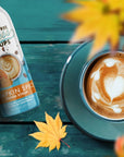 Sugar Free pumpkin spice coffee syrup bottle next to a cup of coffee on a teal surface with autumn leaves.